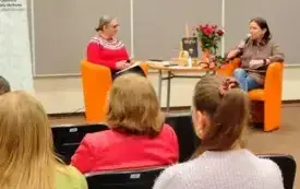 Publiczność zgromadzona w Sali. W tle Agnieszka Kopaczyńska-Moskaluk i Danuta Szulczyńska-Miłosz rozmawiają przy udekorowanym stoliku.