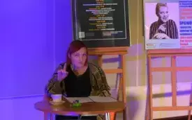 Osoba wyraża zdanie. Znajduje się w otoczeniu plakat&oacute;w.