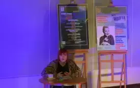 Osoba wyraża zdanie. Znajduje się w otoczeniu plakat&oacute;w.