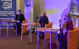 Trzy siedzą przy stolikach. Każdy ma przed sobą mikrofon.
