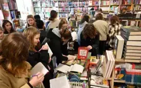 Grupa ludzi znajduje się w Księgarni. Wszyscy sięgają po książki i robią notatki w zeszytach.