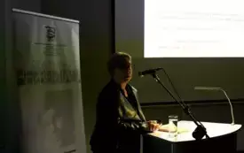 W pomieszczeniu panuje p&oacute;łmrok. Na I planie prof. dr hab. Małgorzaty Mikołajczak.