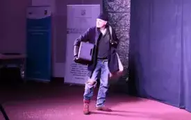 Pomieszczenie doświetlone sztucznym światłem. W centralnej części znajduje się mężczyzna z koszem. 