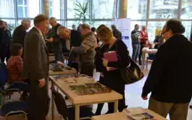 Wydawcy i czytelnicy skupieni wok&oacute;ł stolik&oacute;w, nha kt&oacute;rych ułożone są książki o tematyce regionalnej