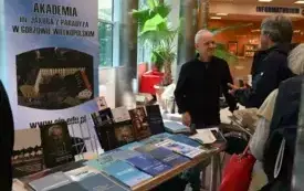 Jacek Lauda rozmawia z czytelnikami przy stoisku Akademii im. Jakuba z Paradyża w Gorzowie. Na stoliku książki wydane przez uczelnię, za nim rollup ze zdjęciem Akademii