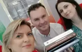 Magdalena Matuszewska, Grzegorz Urbanek i Katarzyna Sanocka-Tureczek pozują do zdjęcia z książkami wydanymii w poprzednim roku w bibliotece