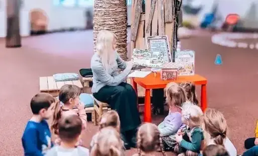 Tytułowe: Bibliotekarka czyta dzieciom książkę podczas zimowych zajęć w bibliotece.
