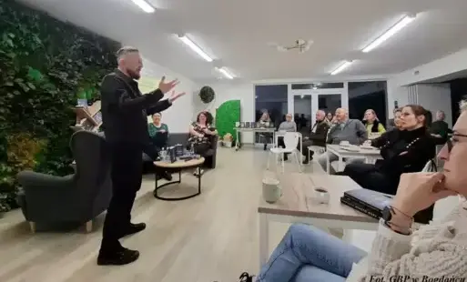 Mężczyzna stoi naprzeciwko siedzących osób.