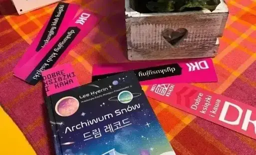 TYTUŁOWE na stole ustawiona jest doniczka z bialymi kwiatkami, książka z zakłądkami