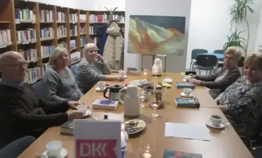 Pięć osób (cztery kobiety i mężczyzna) siedzi przy stole przygotowanym do picia kawy i herbaty oraz do poczęstunku. Na blacie leży kilka egzemplarzy książki pt. „Szklane ptaki” w kolorze morskiej zieleni z pomarańczowymi elementami i żółtym napisem. Twarz