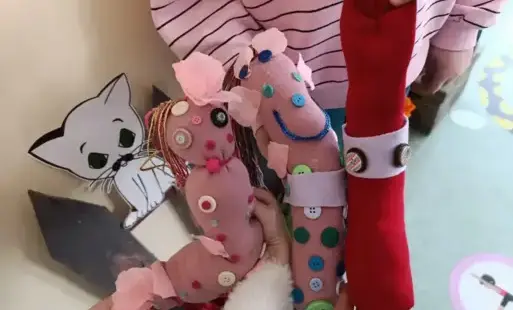 trzy kolorowe maskotki ze skarpetek z naszytymi elementami na tle bluzki