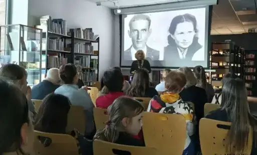 Kobieta na tle ekranu prezencyjnego naprzeciwko siedzącej publiczności.