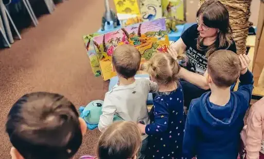 Tytułowe – Bibliotekarka czyta dzieciom książkę o dinozaurach.