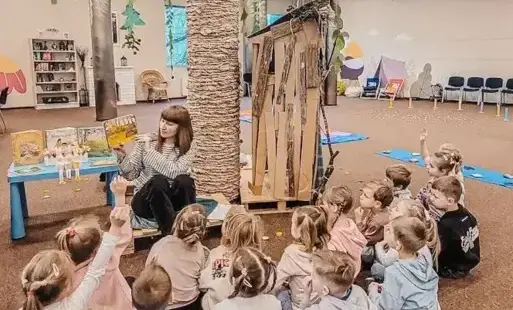 Tytułowe. Pani bibliotekarka czyta dzieciom książkę.