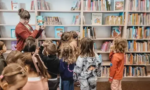 Tytułowe – Bibliotekarka pokazuje dzieciom książkę z regału.