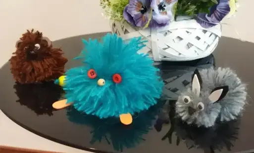 Na czarnym stoliku leżą maskotki z wlóczki, za nimi stroik z kwiatami