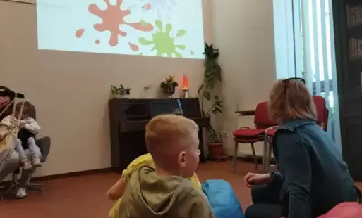 zdjęcie główne - dzieci siedzą na dywanie. Na ścianie wyświetlona prezentacja z kolorami