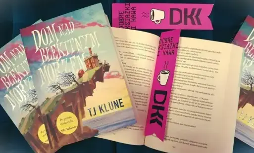 Na stole leżą cztery książki „Dom nad błękitnym morzem”, jedna z nich jest otwarta, a między stronami znajduje się zakładka z logo DKK.