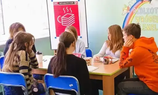 Młodzież przy stole dyskutuje, w tle plakat DKK