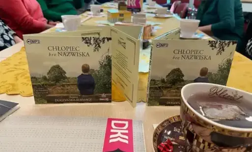 Kilka pudełek od audiobooków stoi na stole, obok filiżanka z herbatą i zakładka DKK.
