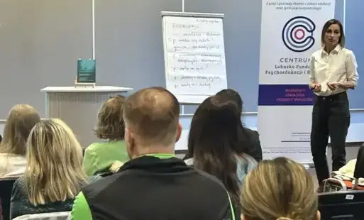 Na zdjęciu widać prowadzącą spotkanie dr Justynę Bucknall-Hołyńską. Niedaleko obok na postumencie stoi książka „Perfekcjonizm: jak uwolnić się od samokrytyki, zbudować stabilne poczucie własnej wartości i odnaleźć wewnętrzną równowagę” Sharon C. Martina. 