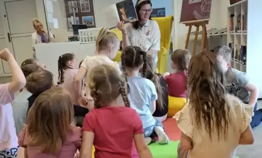 Kobieta prezentuje książkę wśród siedzących słuchaczy.