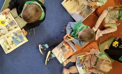 Dzieci siedzą na podłodze na kolorowych poduchach i oglądają książeczki.