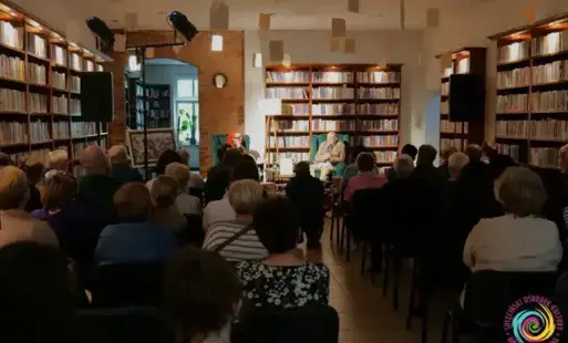 Dwie osoby na fotelach naprzeciwko siedzących słuchaczy.