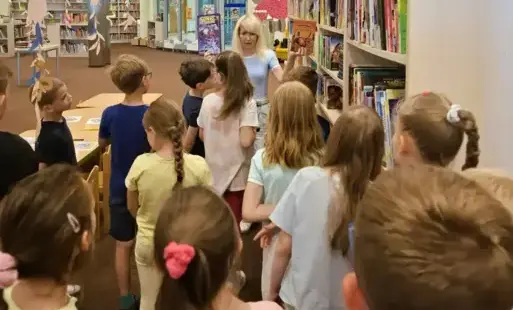Bibliotekarka pokazuje dzieciom różne książki z księgozbioru.