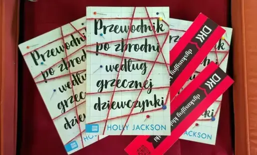 Na bordowym tle leżą trzy książki Holly Jackson „Przewodnik po zbrodni według grzecznej dziewczynki” oraz dwie różowe zakładki z logo DKK.