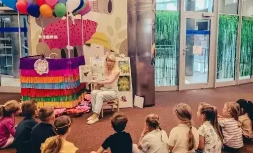 Tytułowe: Bibliotekarka czyta dzieciom książkę podczas lekcji bibliotecznej.