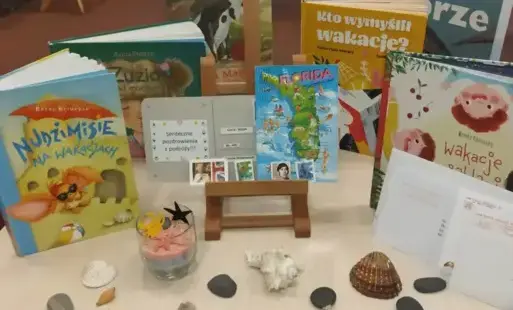 prezentacja książek związanych z wakacjami, dookoła rozłożone muszelki, kamyczki i praca plastyczna do wykonania