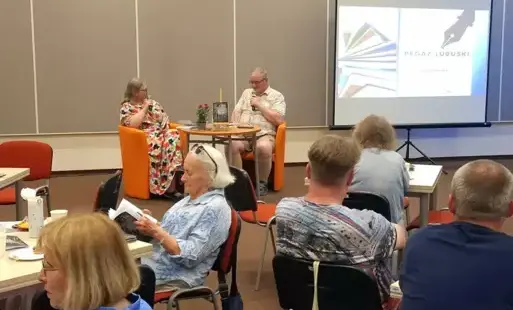 Agnieszka Kopaczyńska-Moskaluk oraz Ferdynand Głodzik siedzą przed publicznością i przemawiają do mikrofonów. W tle na ekranie wyświetlana jest prezentacja.