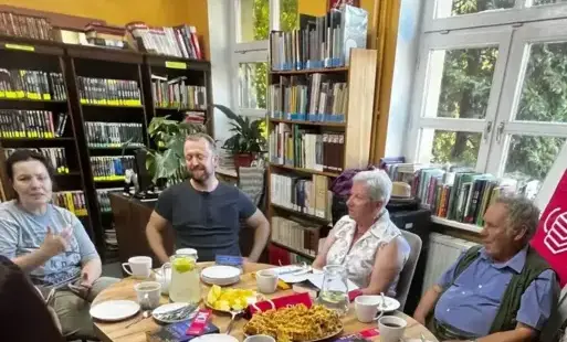 Uczestnicy DKK podczas spotkania, wszyscy siedzą przy stole. W tle regały na książki.