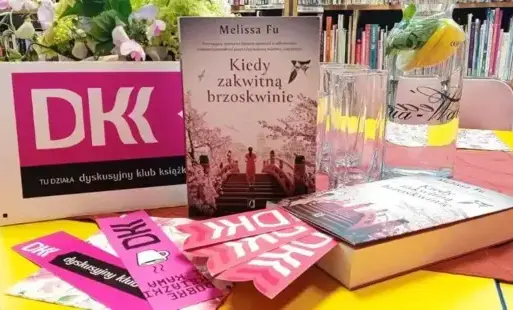Tytułowe - Na stole książki, baner DKK i zakładki do książek, w tle karawka z wodą