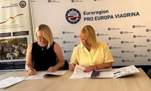Dwie kobiety podpisują dokumenty przy stole.
