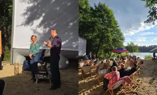 Kobieta i mężczyzna przy ekranie na plaży nad jeziorem, publiczność siedzi na leżakach.