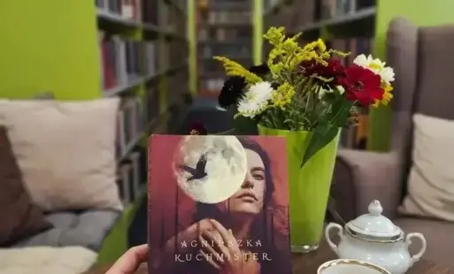 fragment zdjęcia przedstawia wnętrze biblioteki z rzędami regałów wypełnionych książkami w tle.