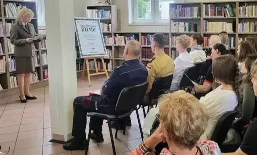 Grupa osób siedzi w pomieszczeniu bibliotecznym, słuchają kobiety w mundurze leśnika