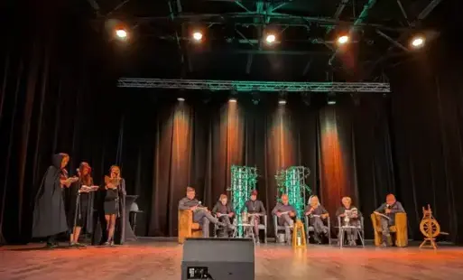 Grupa osób na scenie teatralnej podczas publicznego czytania.