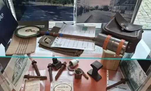 Przeszklona gablota wystawowa z historycznymi eksponatami kolejowymi, które są ułożone na dwóch poziomach.