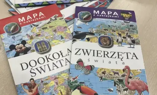 Na stole leżą mapy z naklejkami: Dookoła świata i Zwierzęta świata oraz broszura zatytułowana Moje relacje w Internecie.
