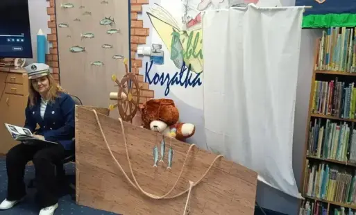 Tytułowe - Kobieta w stroju marynarskim z książką oraz makieta statku z żaglem.