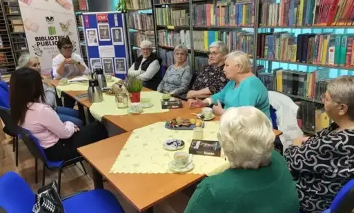 W pomieszczeniu biblioteki przy stole siedzą członkowie Klubu i rozmawiają