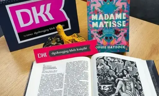 Tytułowe – Okładka książki na stole druga książka otwarta na reprodukcji i logo DKK