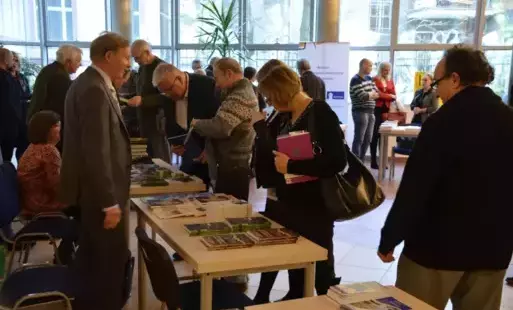 Wydawcy i autorzy zgromadzeni przy stolikach w sali nr 8. Wśród nich przemawia jeden z autorów, stojąc