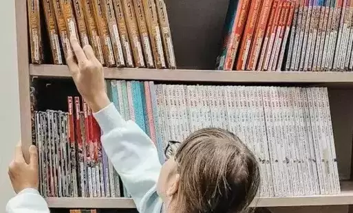 Tytułowe. Dziewczynka przegląda książki ustawione na regałach.