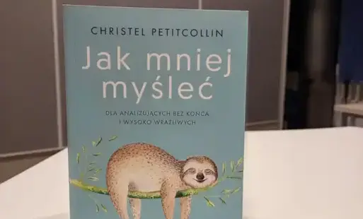 Na zdjęciu widoczna jest książka Ch. Petitcollin ' Jak mniej myśleć. Dla analizujących bez końca i wysoko wrażliwych'. Książka ma niebieską okładkę, na której widać uśmiechniętego leniwca.