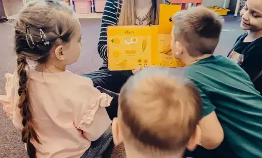 Bibliotekarka czyta dzieciom pachnącą książkę o owocach.