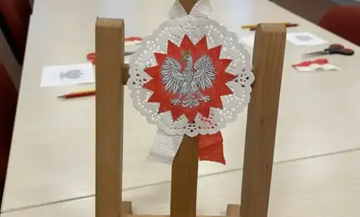 Na długim stole minisztaluga drewniana z kotylionem, w tle materiały plastyczne.